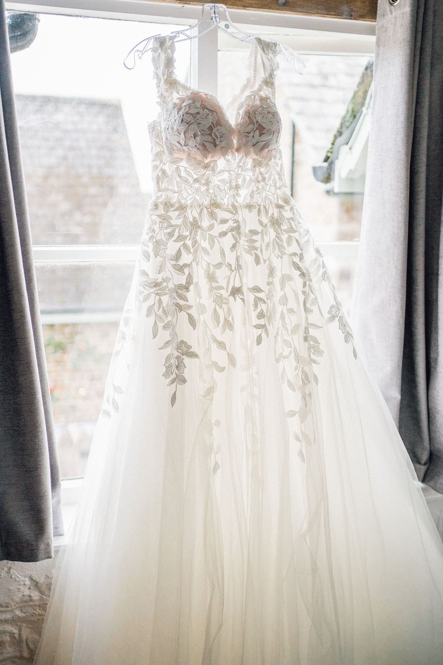 Elegant white wedding dresses with delicate lace details hanging in a row against a window with natural light.