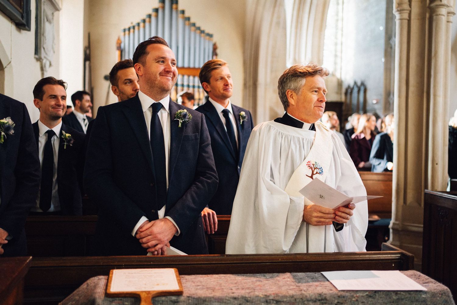 A group of formally dressed people stand at the altar in a church during a wedding ceremony.