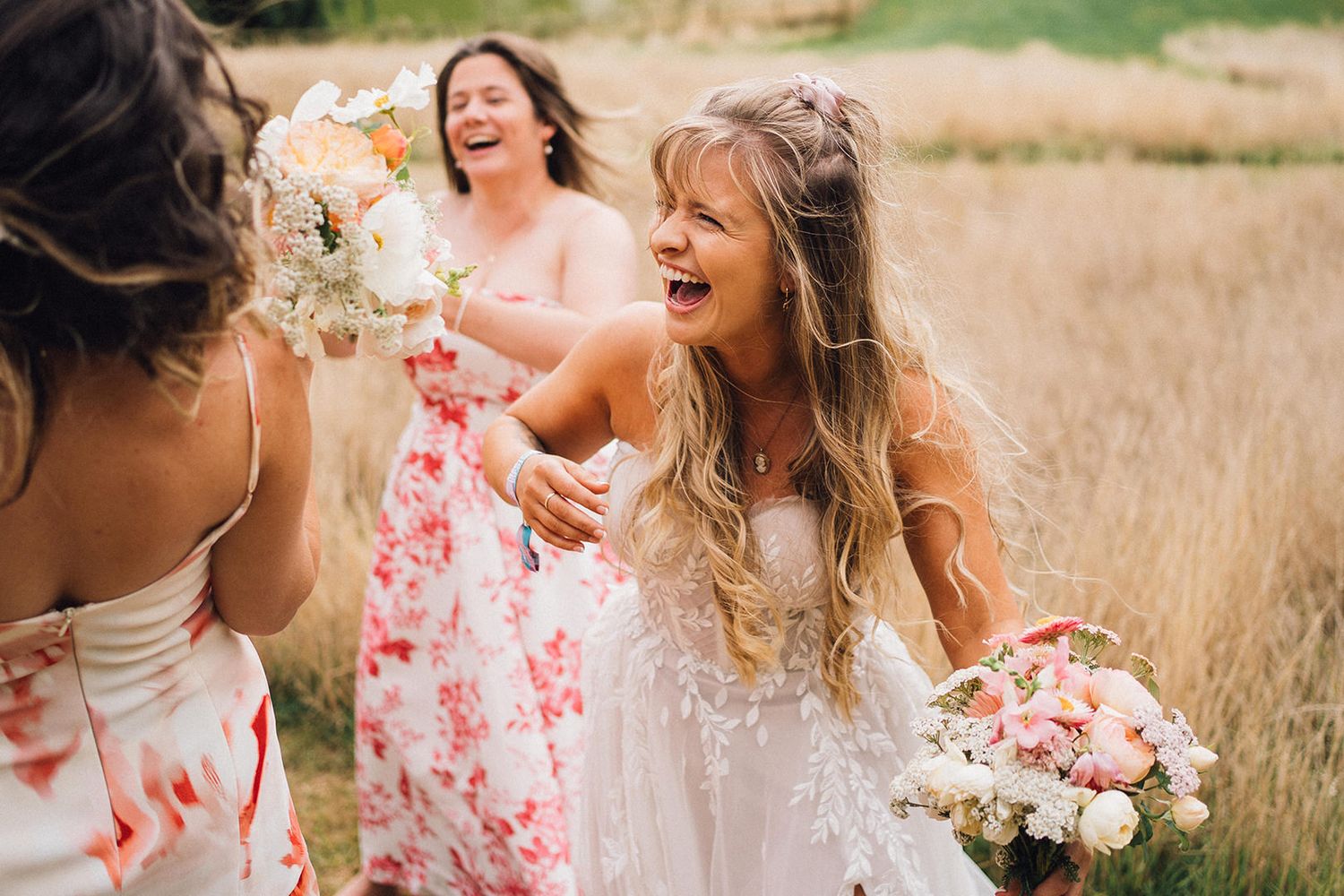Group wearing floral dresses poses together in a sunlit field of tall grass.