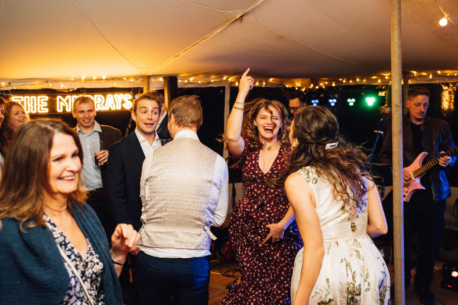 People dancing and celebrating at a lively evening party under a tent with festive lighting.