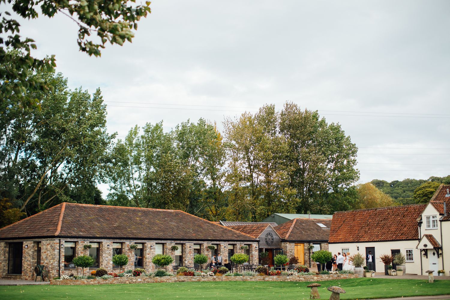 Rustic stone barn wedding venue with manicured gardens and mature trees in the English countryside.