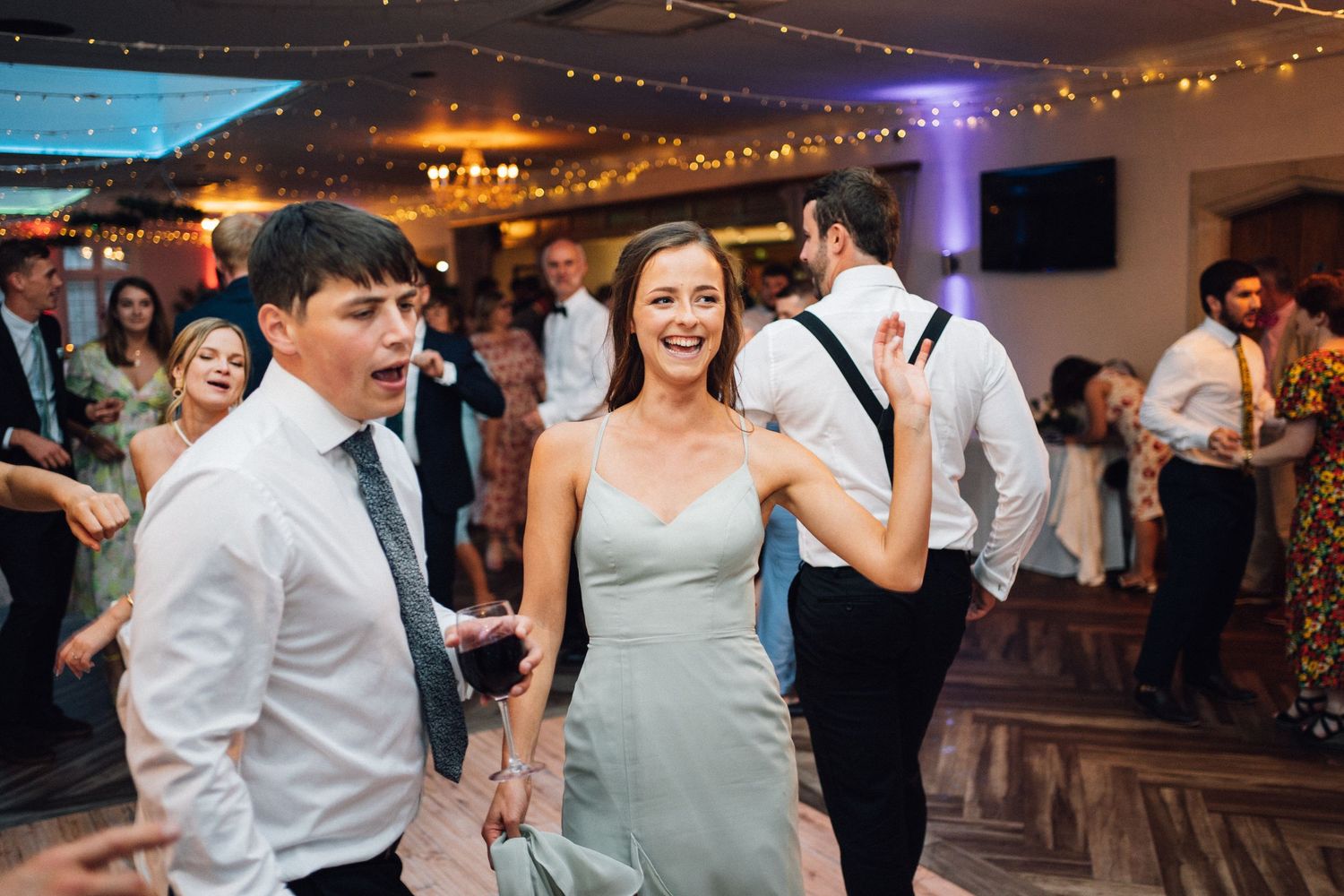 Wedding reception dance floor filled with guests celebrating under string lights.