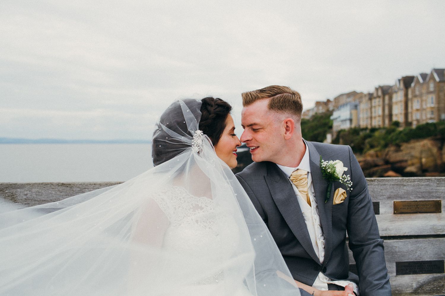 A couple in wedding attire shares romantic moments along a scenic waterfront during their special day.