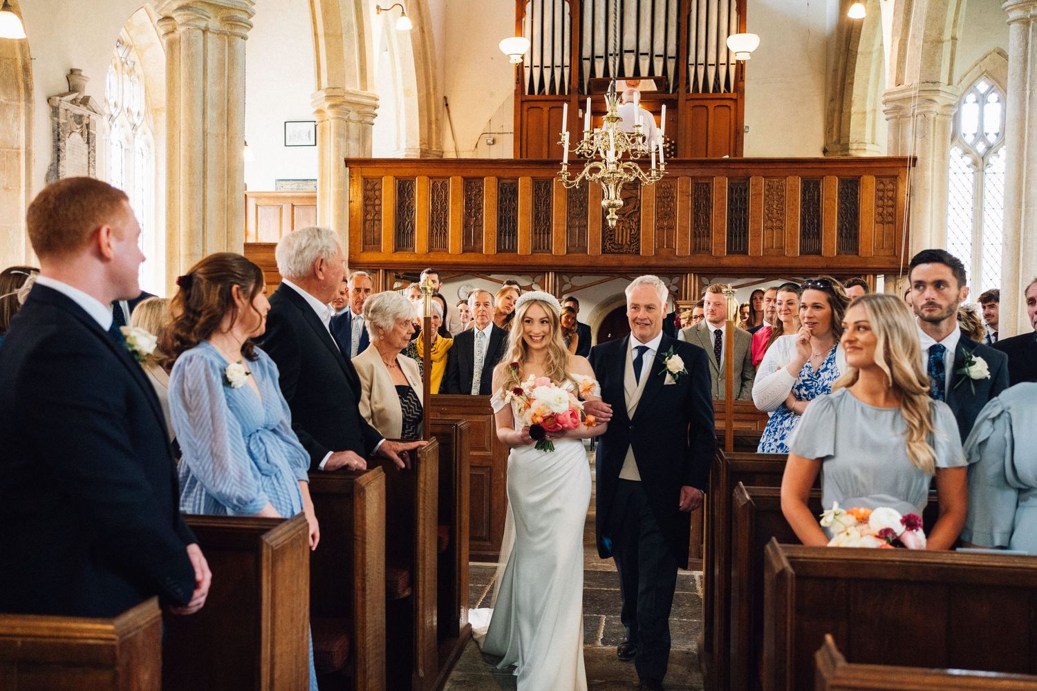 Wedding guests celebrate joyfully in a traditional church setting with wooden pews and ornate architecture.