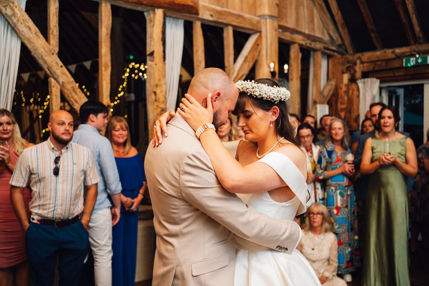 Wedding couple shares their first dance surrounded by guests in a rustic barn venue with wooden beams.