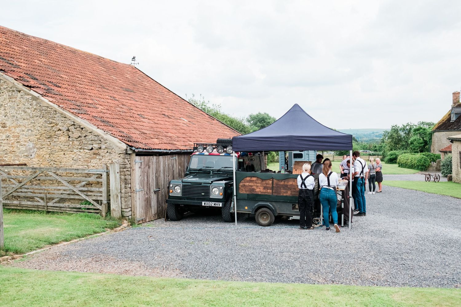 Stone barn exterior with gravel courtyard and guests gathering under outdoor tent.