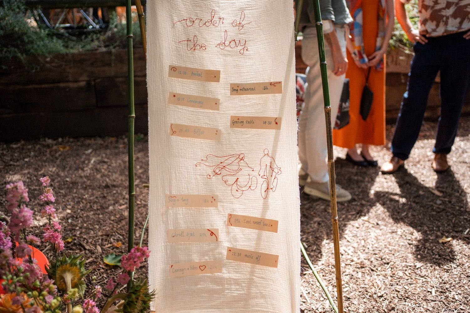 Rustic wedding order of the day sign on linen fabric displayed outdoors at a garden ceremony.