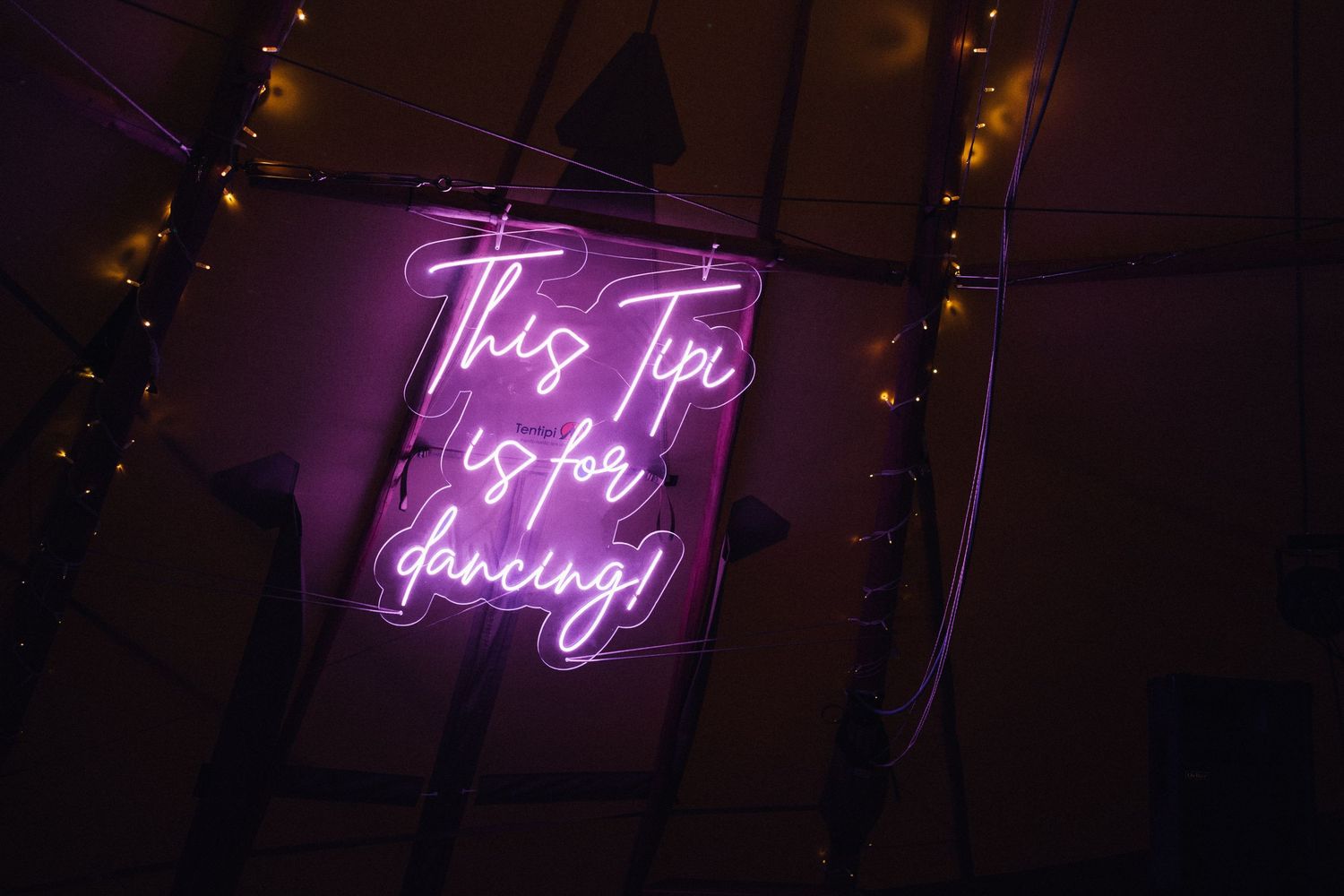 Purple neon sign reading 'Tip Top Through' glowing in dark room with string lights.