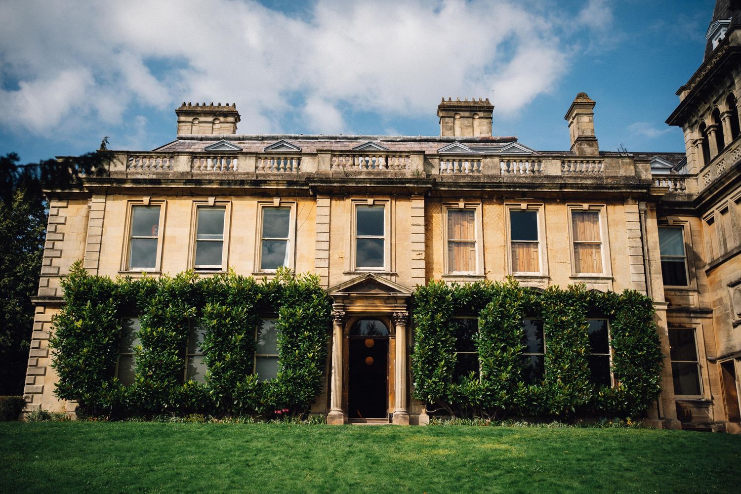 Elegant Georgian stone manor house with ivy-covered facade and manicured lawn under blue sky.