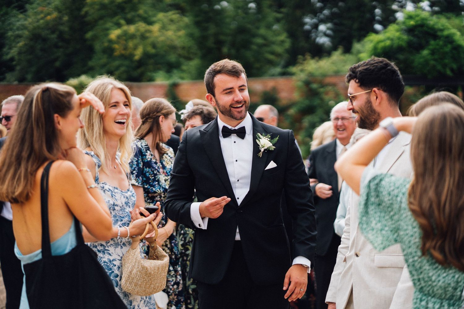 Wedding guests mingle and socialize outdoors during a formal celebration in a garden setting.