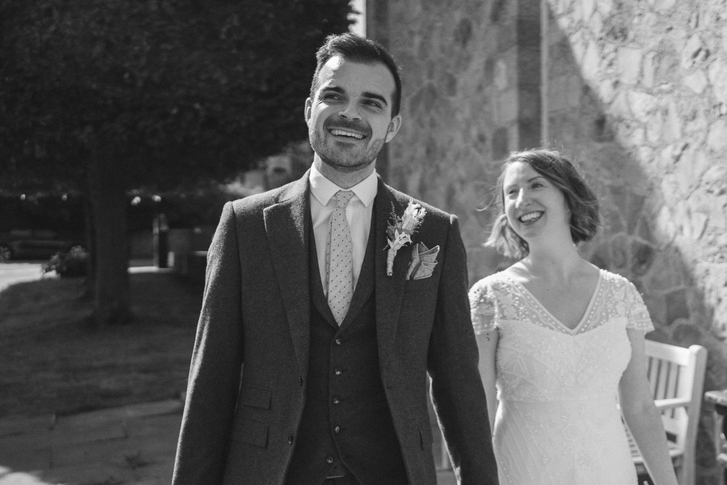 A joyful bride and groom share a candid moment walking together in black and white photography.
