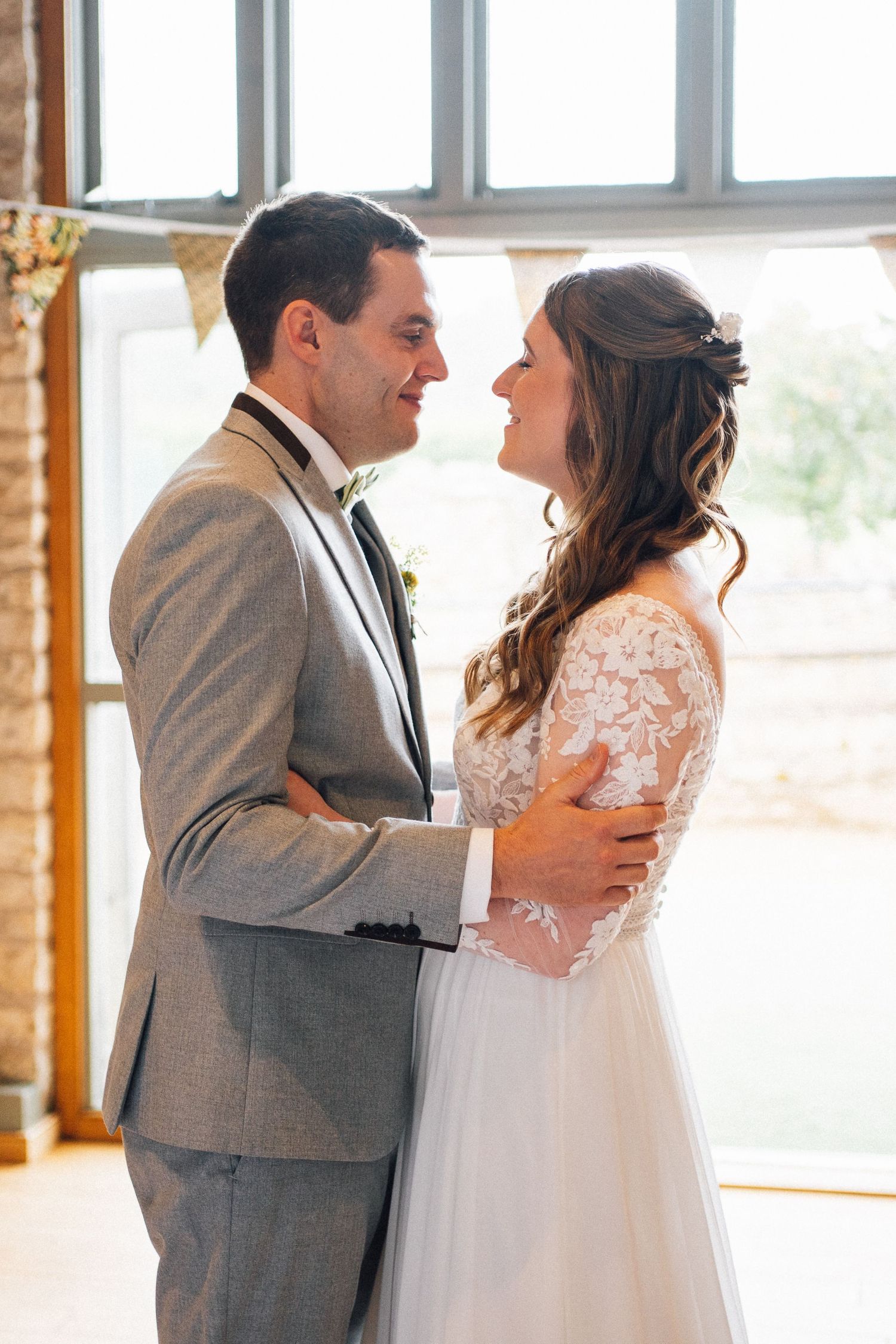 Couple shares an intimate first look moment in a sunlit room with rustic wooden beams.