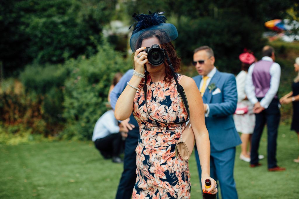 Wedding guests mingling at an outdoor garden reception on a sunny day.