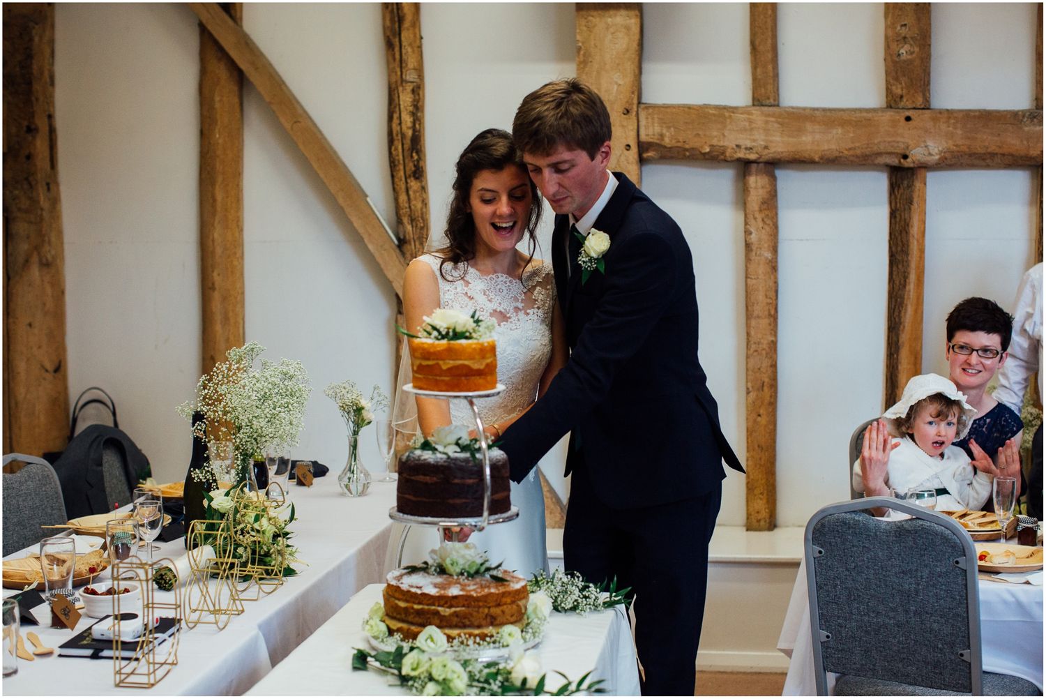 Wedding cake display at rustic reception venue with wooden beam decor.