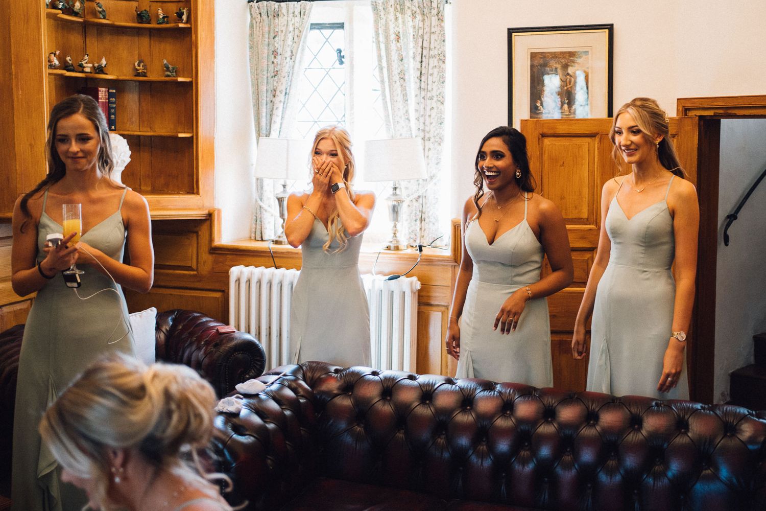 Bridesmaids in matching silver dresses share excited reactions in an elegant room.