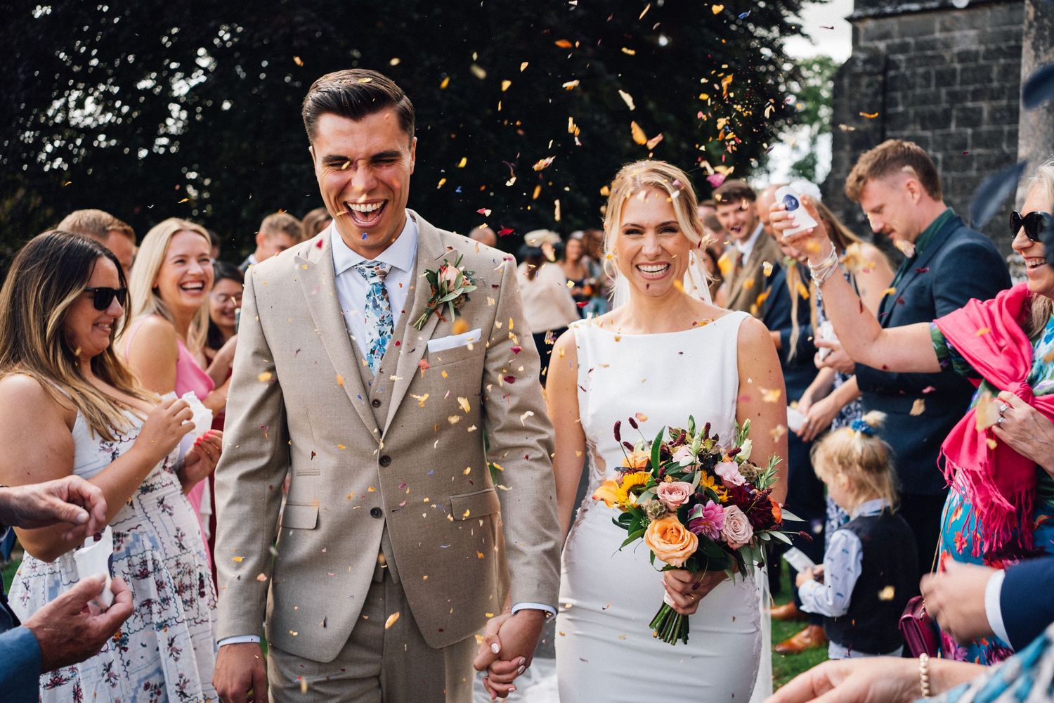 Joyful wedding celebration with confetti toss outside historic stone building.