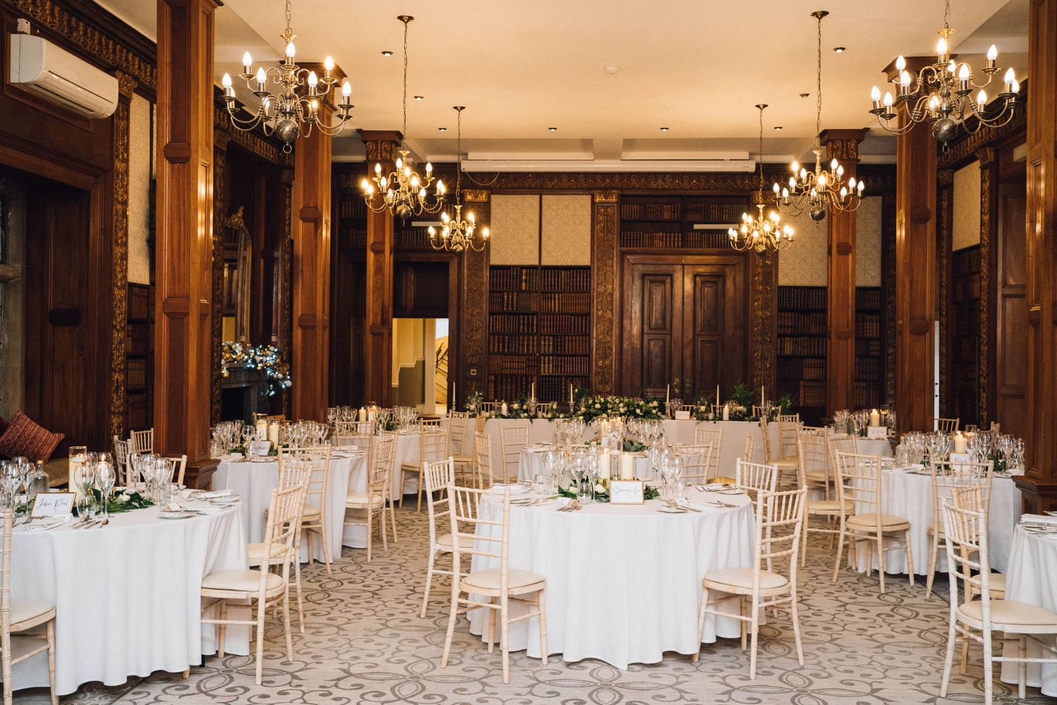Panoramic view of an elegant wedding reception hall with white linens and chandeliers.