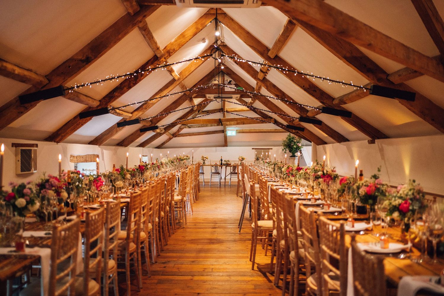 Panoramic view of a barn reception hall with exposed wooden beams and romantic lighting.