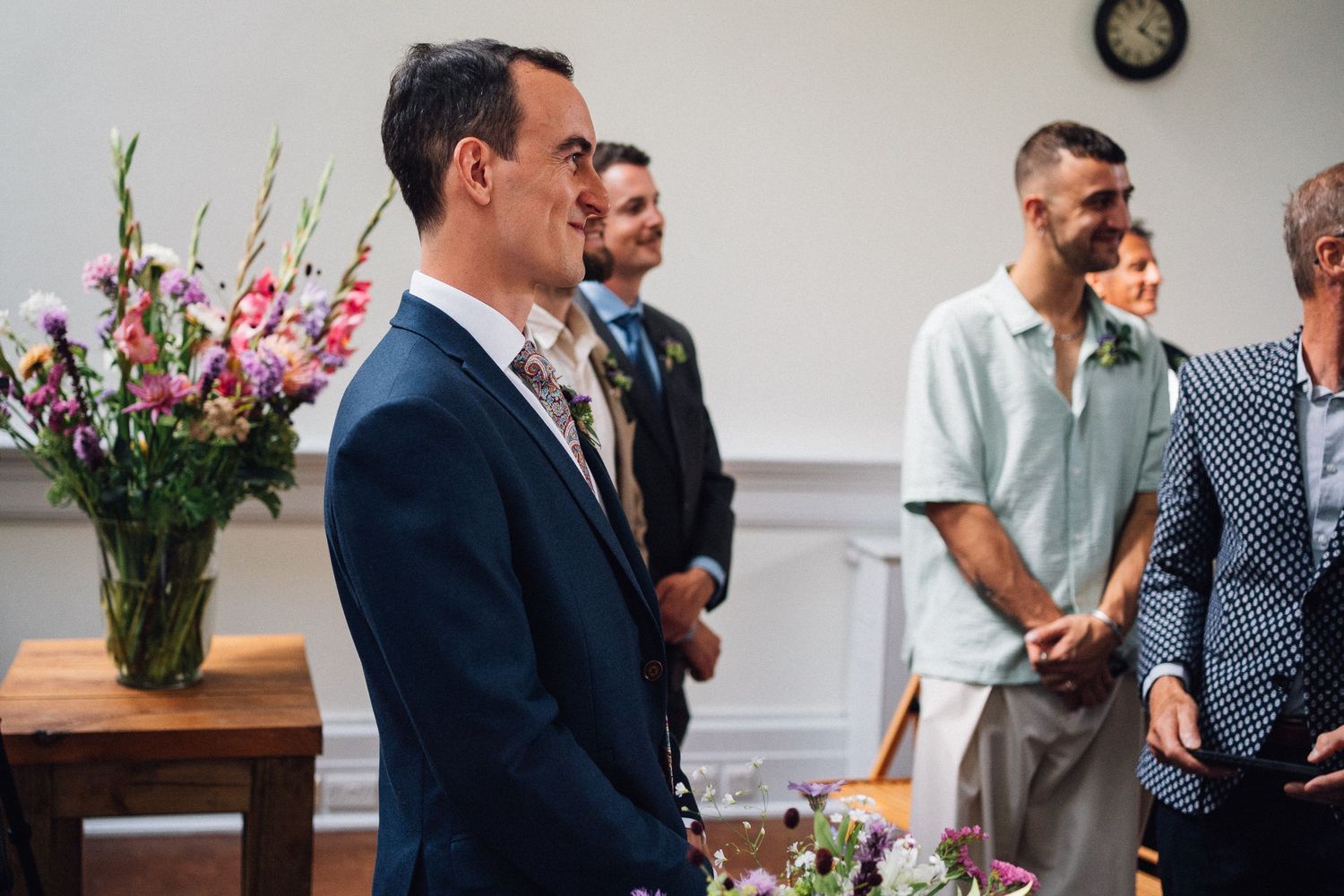 People gather at a wedding ceremony with pink floral arrangements and elegant decor in an indoor venue.