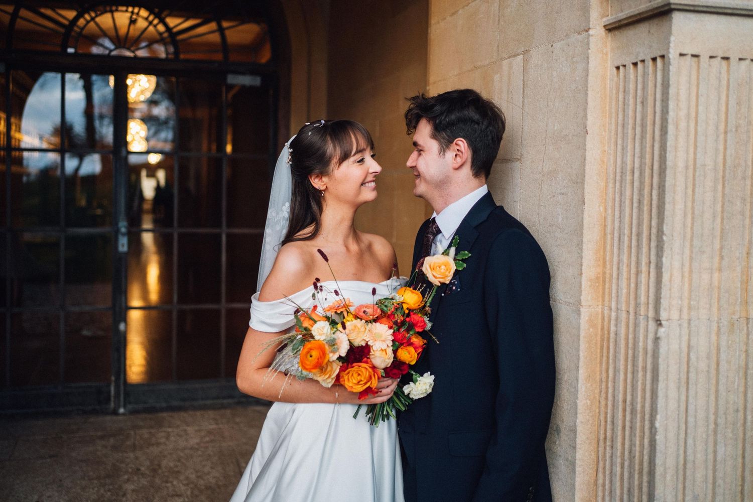 A couple shares an intimate moment during their wedding at a historic venue with stone columns and warm lighting.