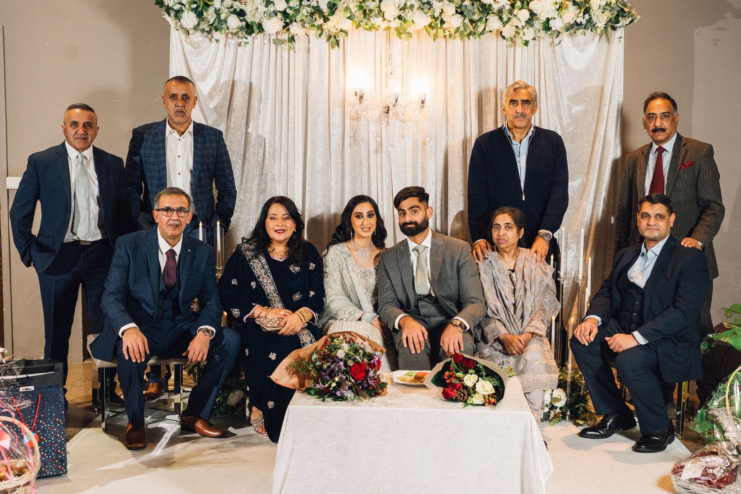 Large group photo of wedding guests seated together on couches with floral decorations.