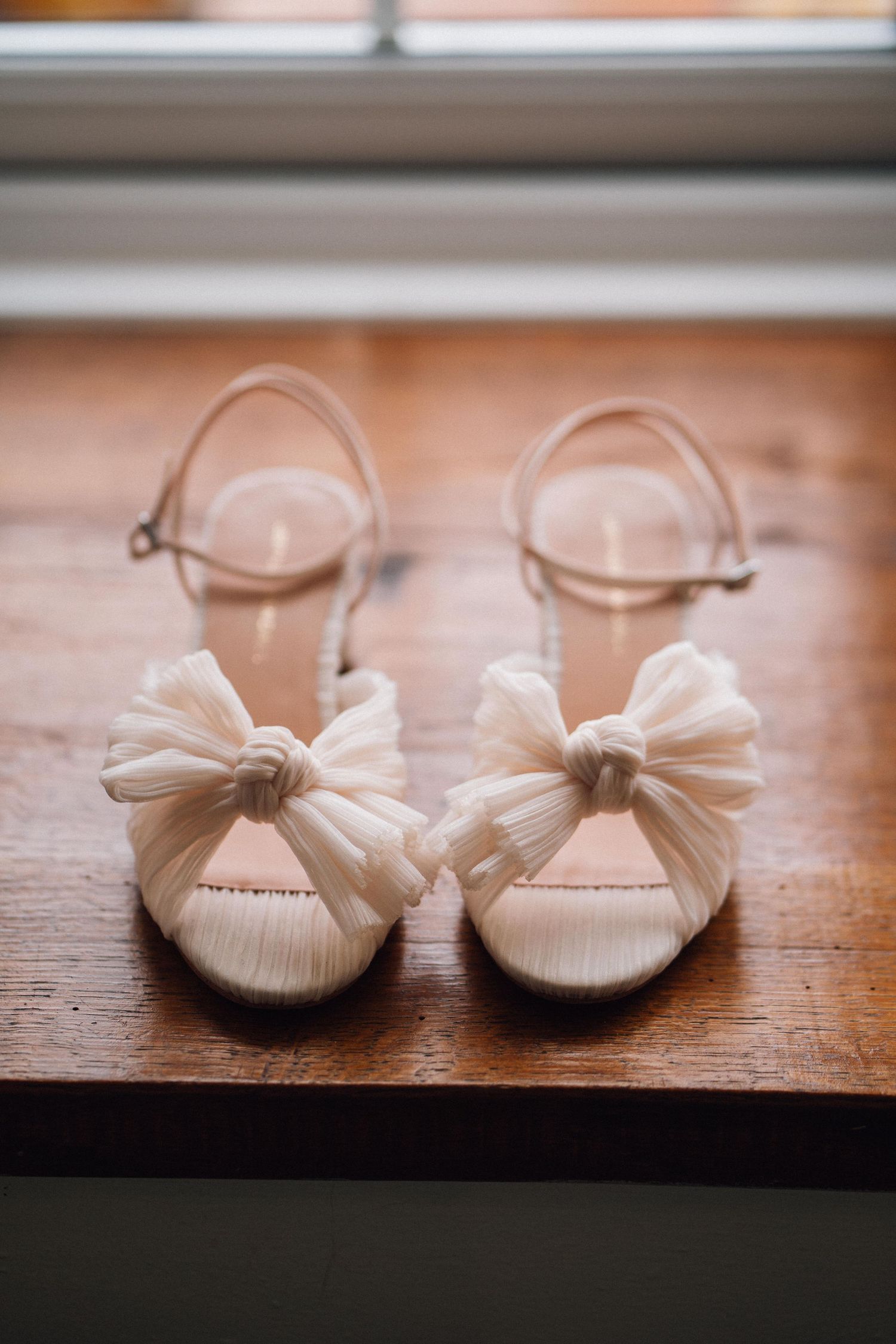 Delicate white ballet flats with bow details displayed on a polished wooden surface.