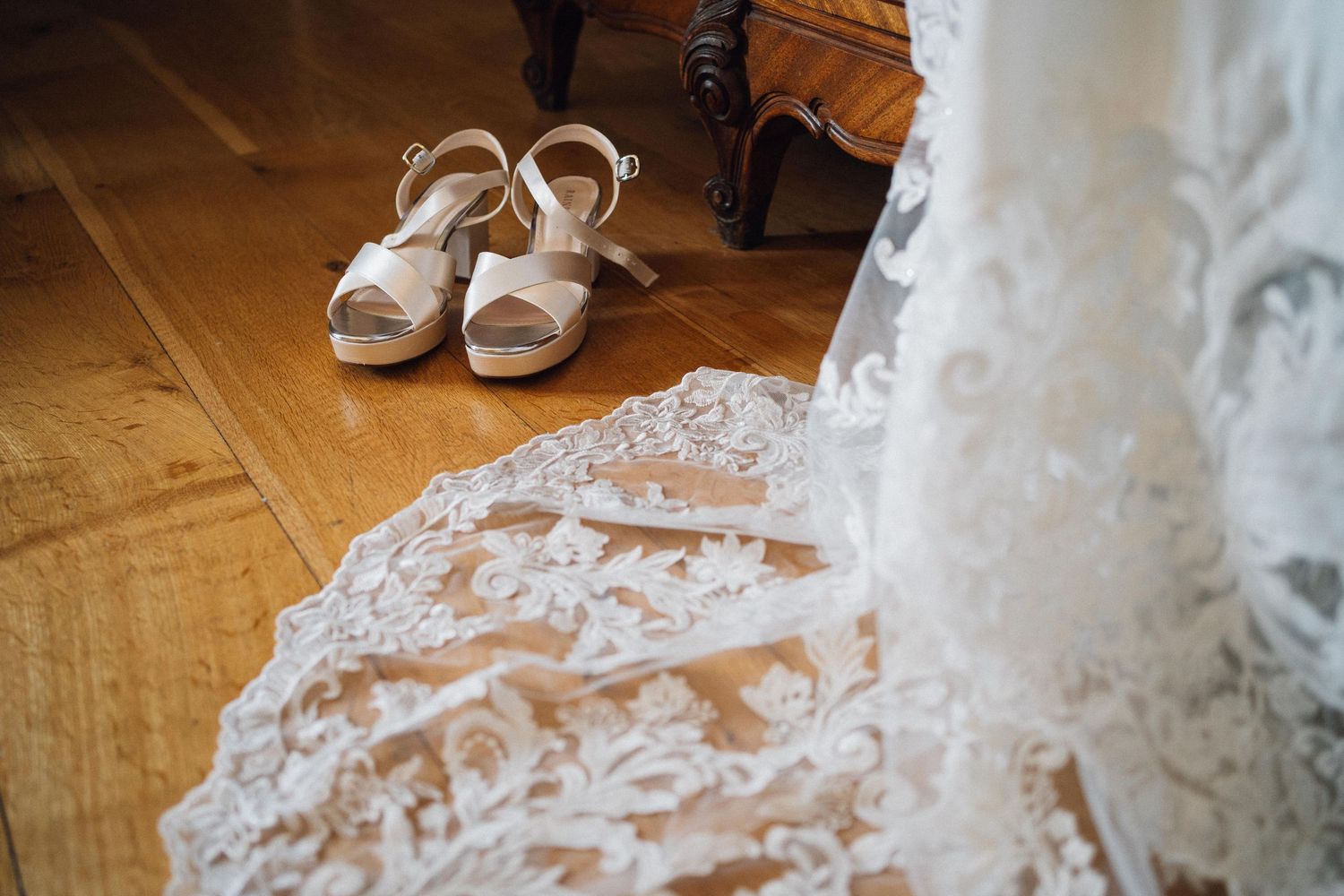 White bridal shoes and delicate lace wedding dress details on wooden floor create an elegant wedding day setting.
