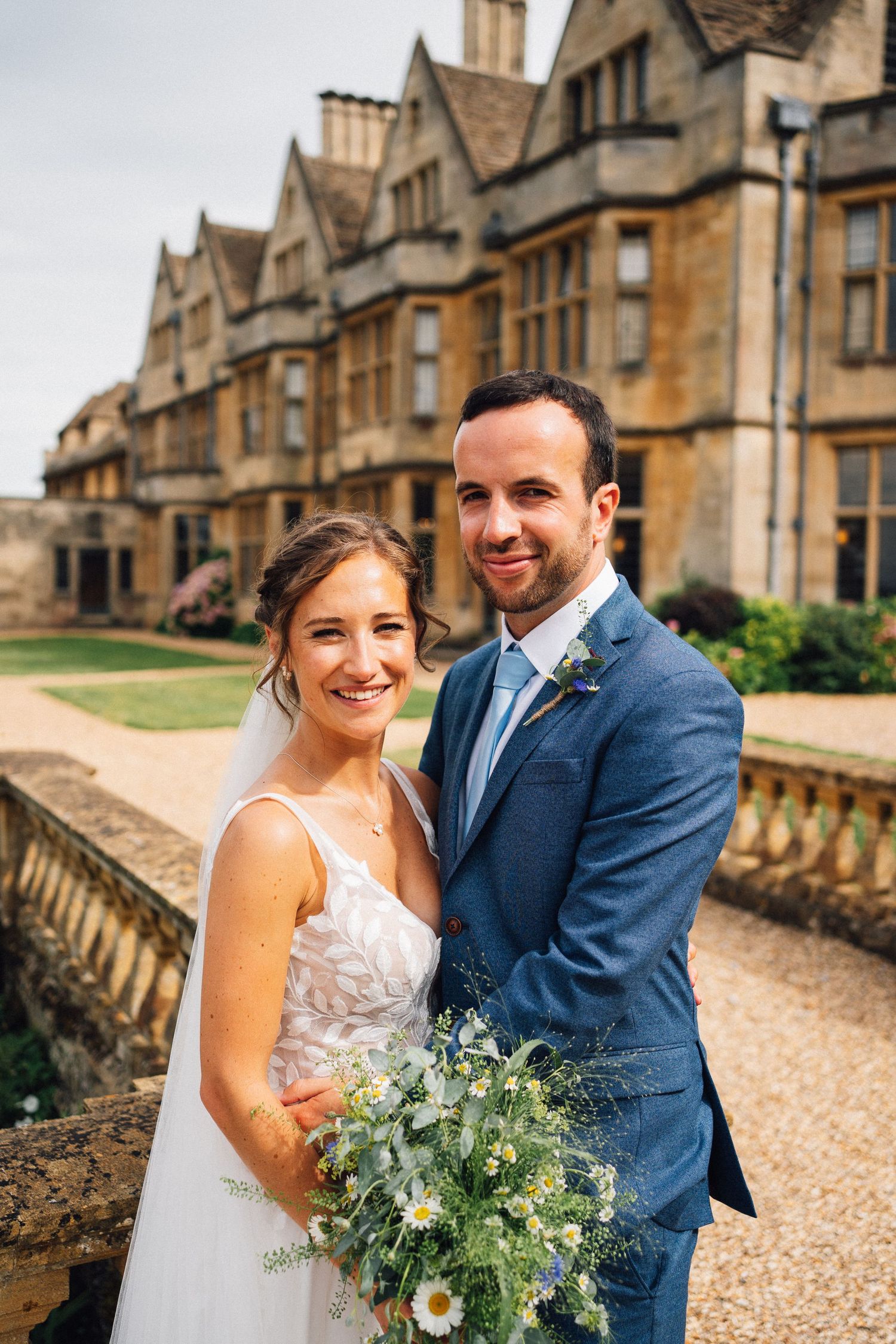 A couple poses together against a historic stone manor building in warm golden light.
