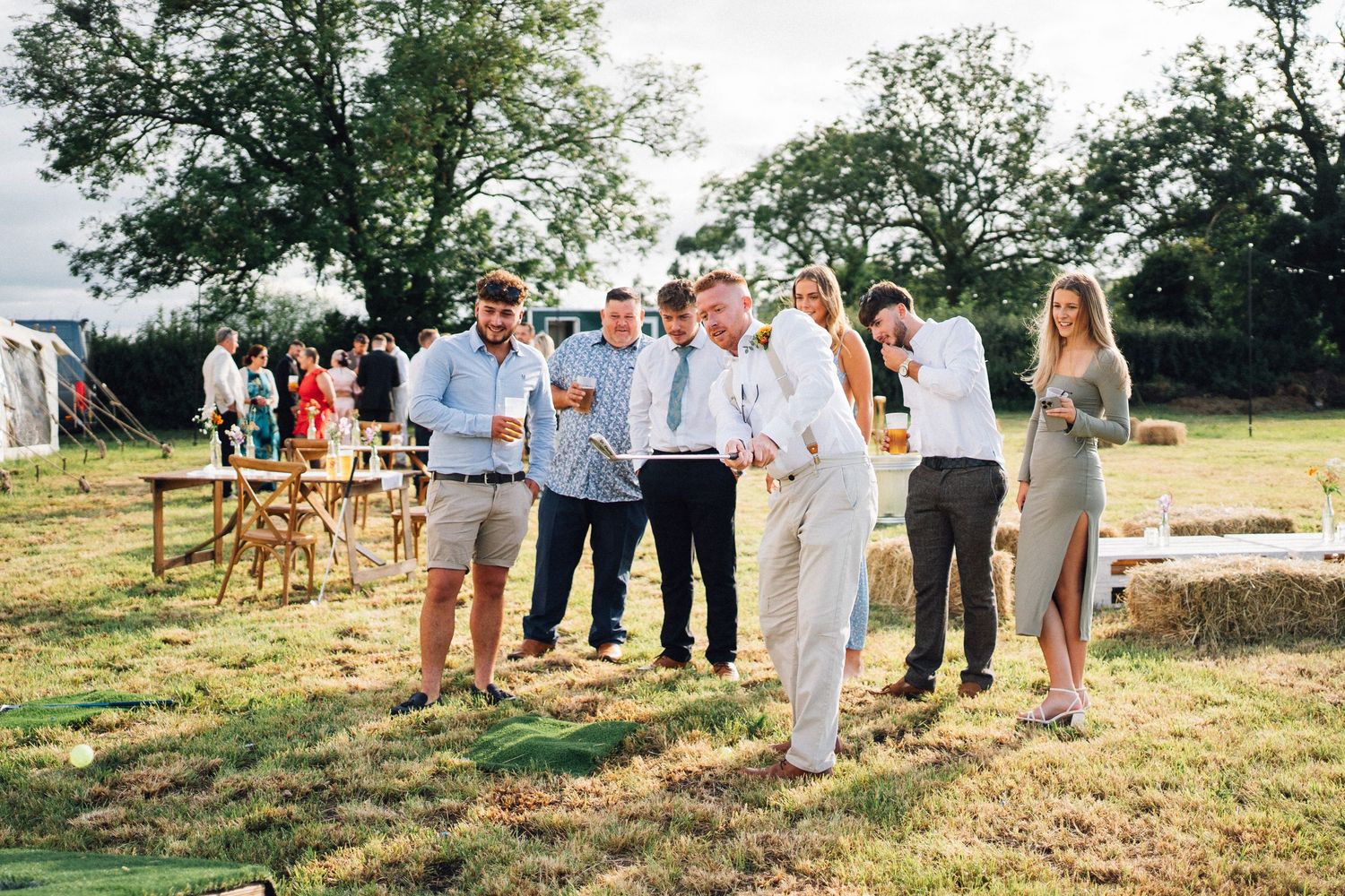 Wedding guests in white attire gather on a grassy hillside during an outdoor summer celebration.