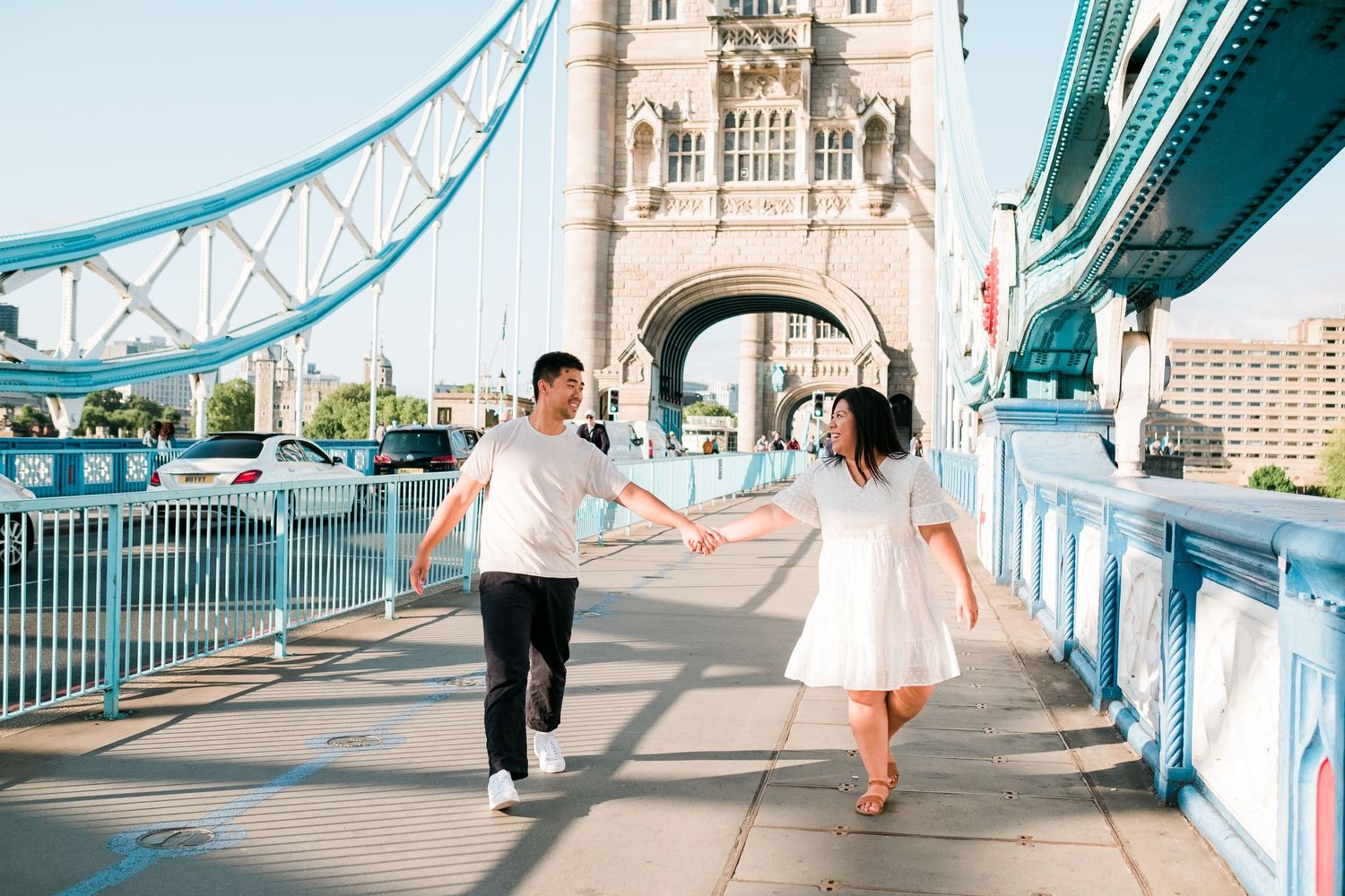 A couple strolls across the iconic Tower Bridge in London with its distinctive turquoise metalwork.