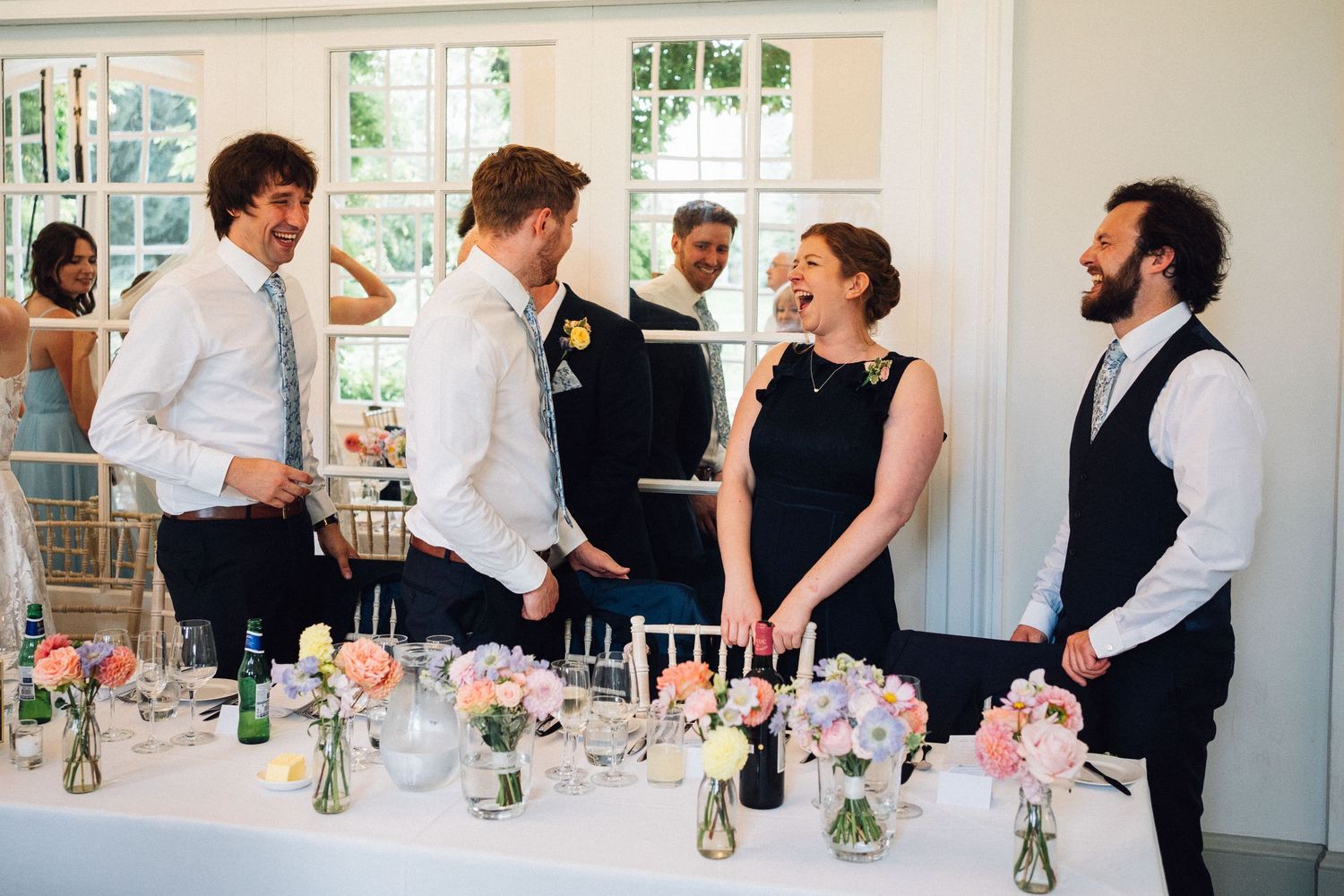 Wedding reception tables adorned with delicate pink floral arrangements and glassware in a bright indoor space.