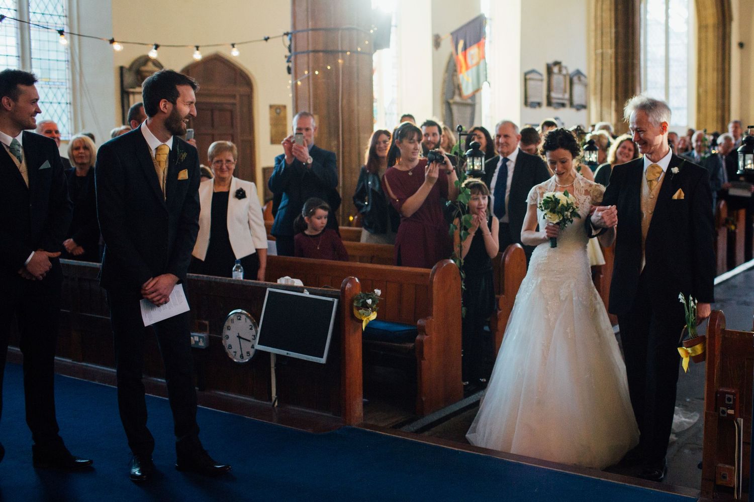Wedding ceremony in traditional church setting with guests watching from wooden pews.
