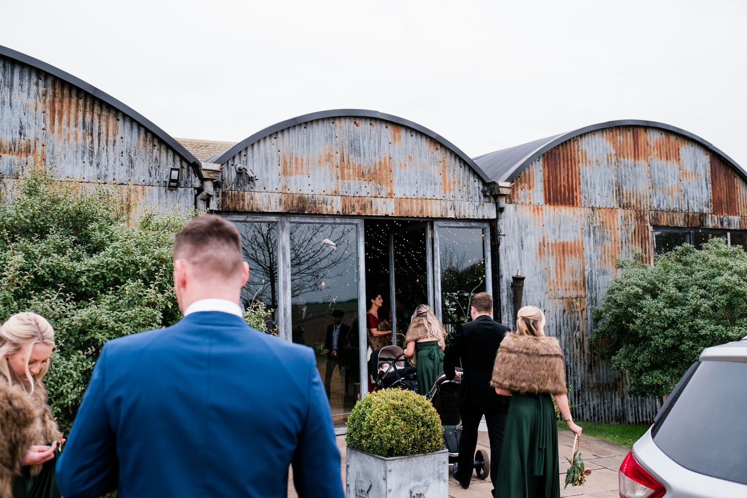 Wedding venue exterior featuring industrial-style curved metal buildings and landscaped grounds.