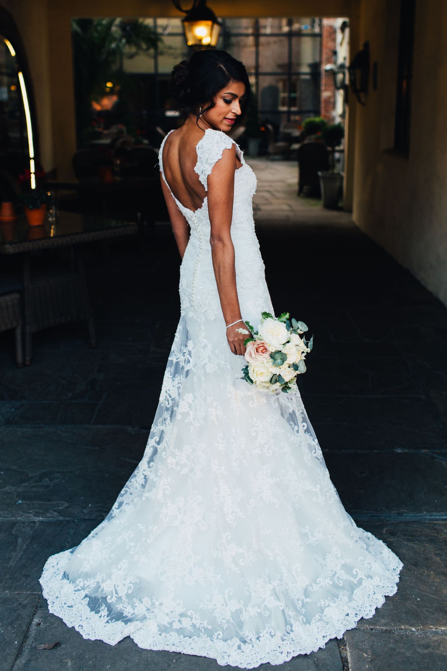 A stunning white lace wedding dress with a flowing train is showcased against a dark background.