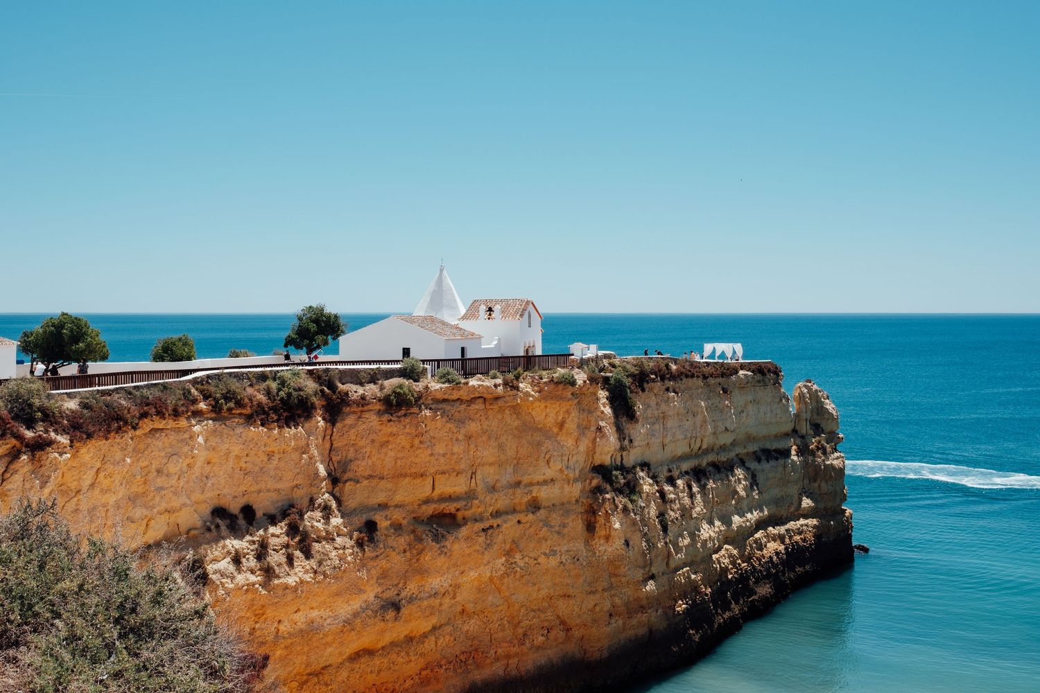 White church perched on orange limestone cliffs overlooking the blue Atlantic Ocean in Portugal.