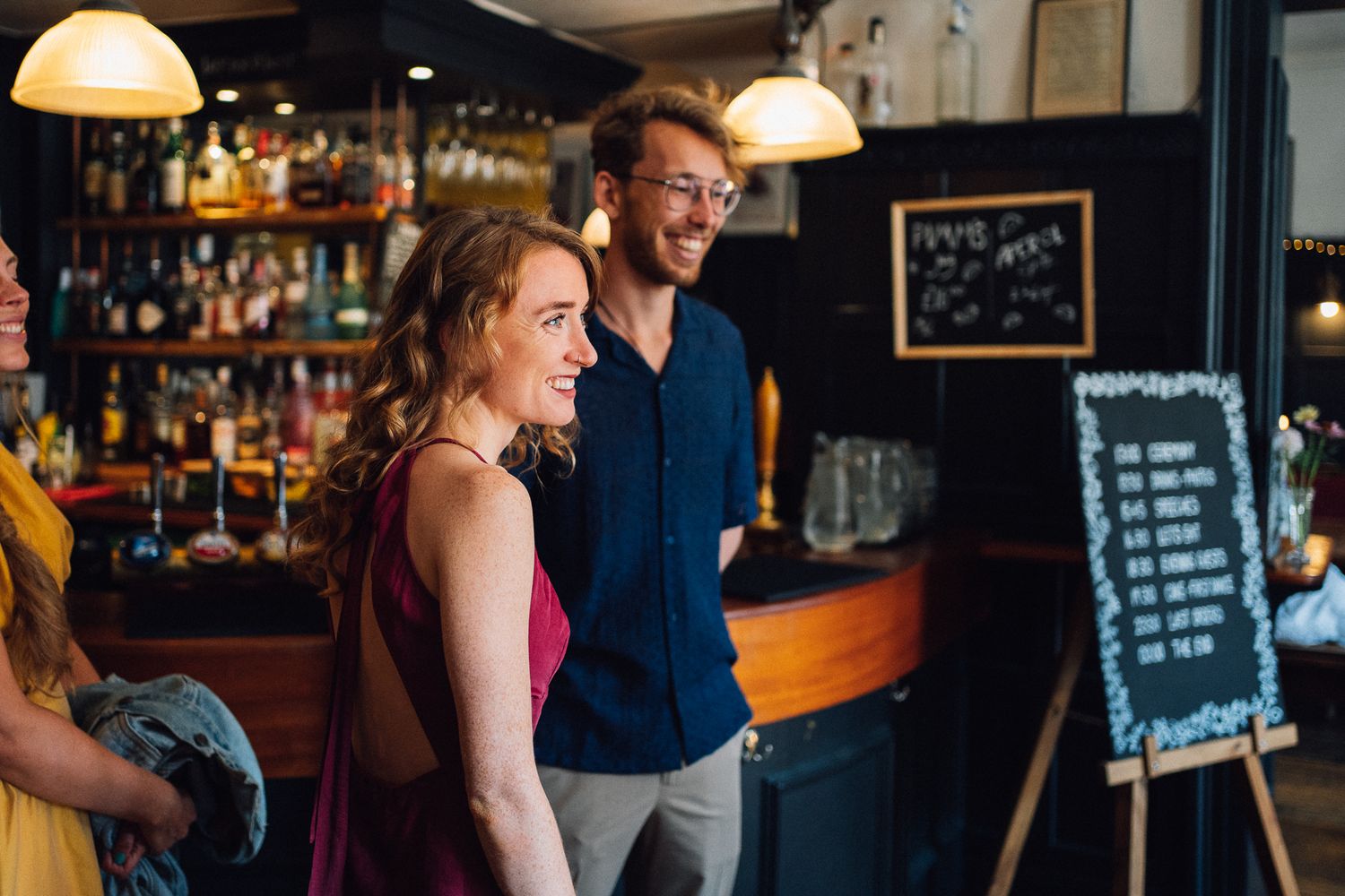 People enjoying drinks and socializing at a lively bar with warm lighting and chalkboard menus in the background.