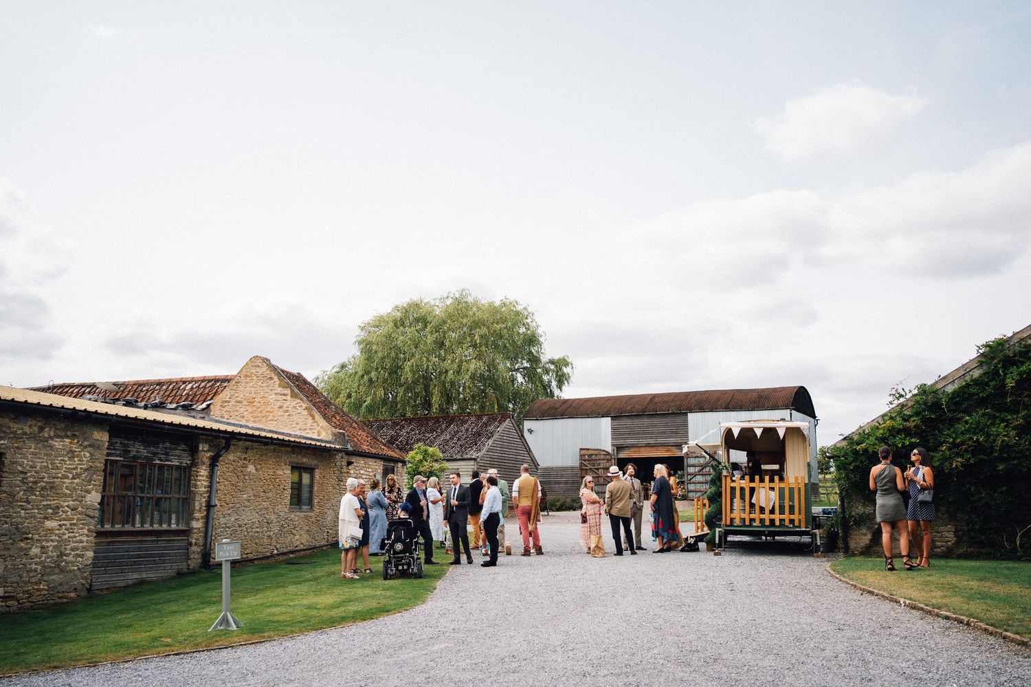 A rustic barn venue with stone buildings and guests gathered outside on a cloudy day.
