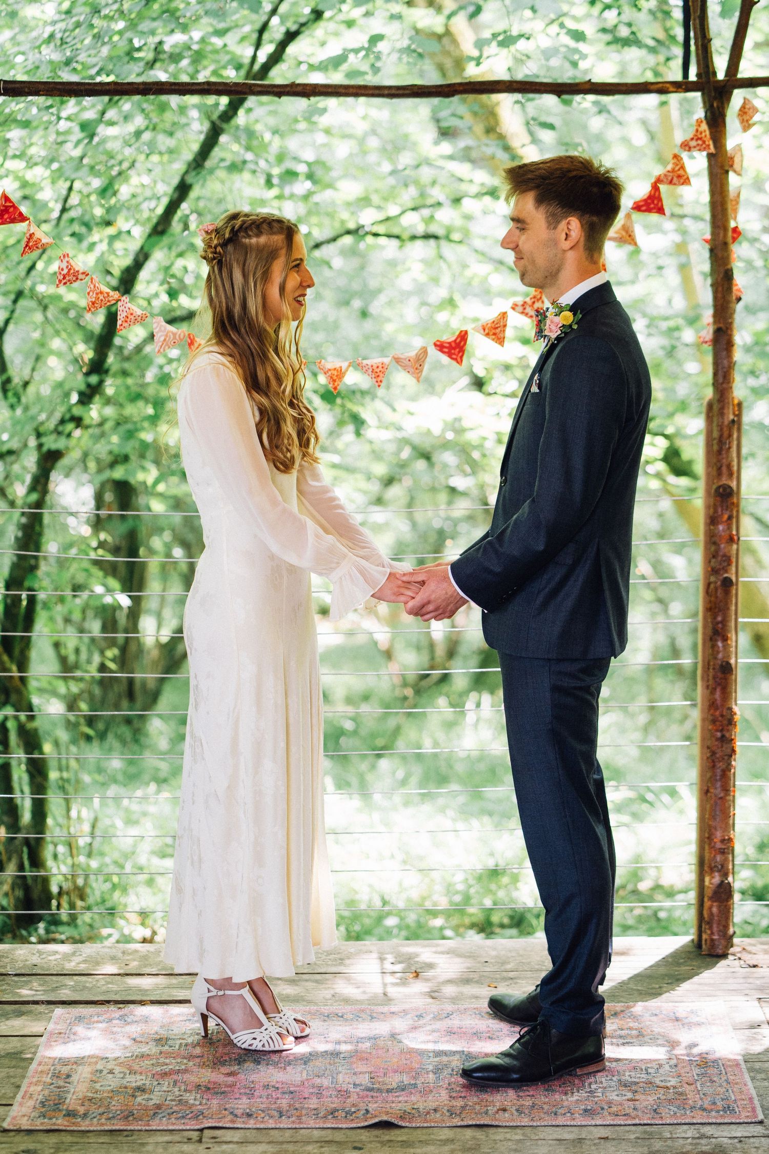 Two children in formal attire stand on a vintage rug under festive bunting at an outdoor celebration.