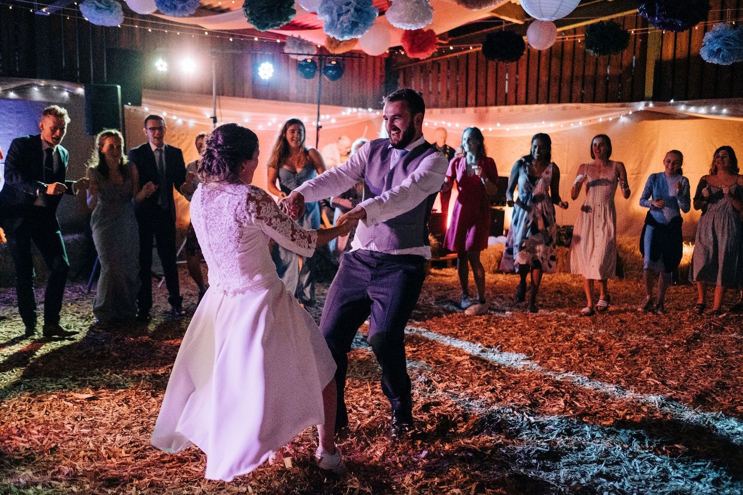Couple dancing on confetti-covered floor during wedding reception under paper lantern decorations.
