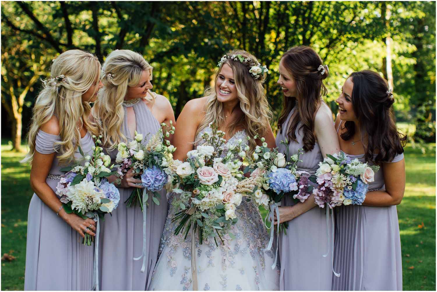 Bridal party in lavender dresses holding white and blue floral bouquets.