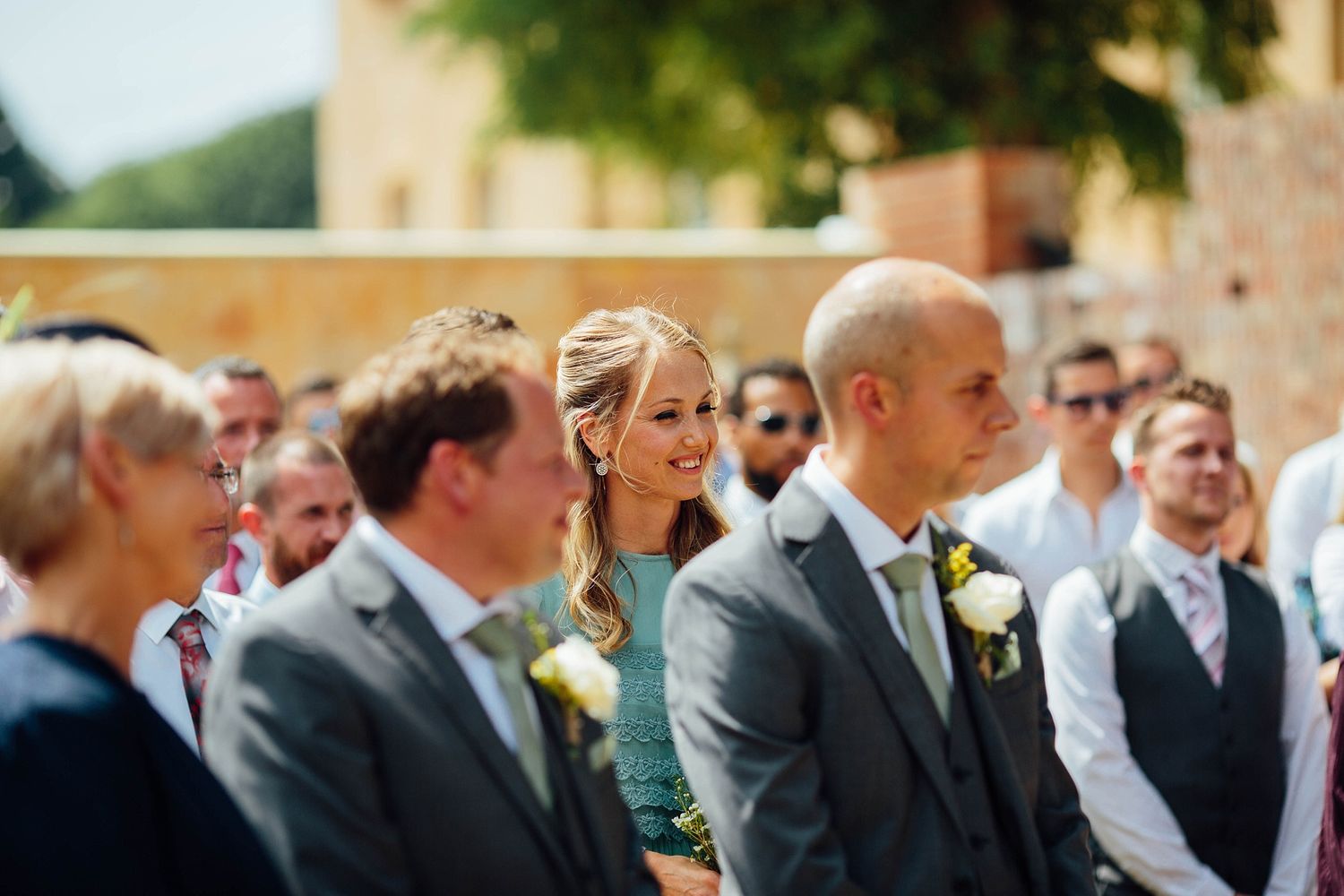Wedding guests seated in rows at an outdoor garden venue with brick walls.