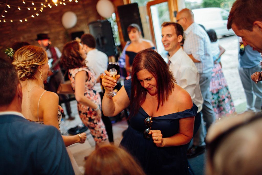 Wedding guests dancing and celebrating on dimly lit dance floor with string lights overhead.
