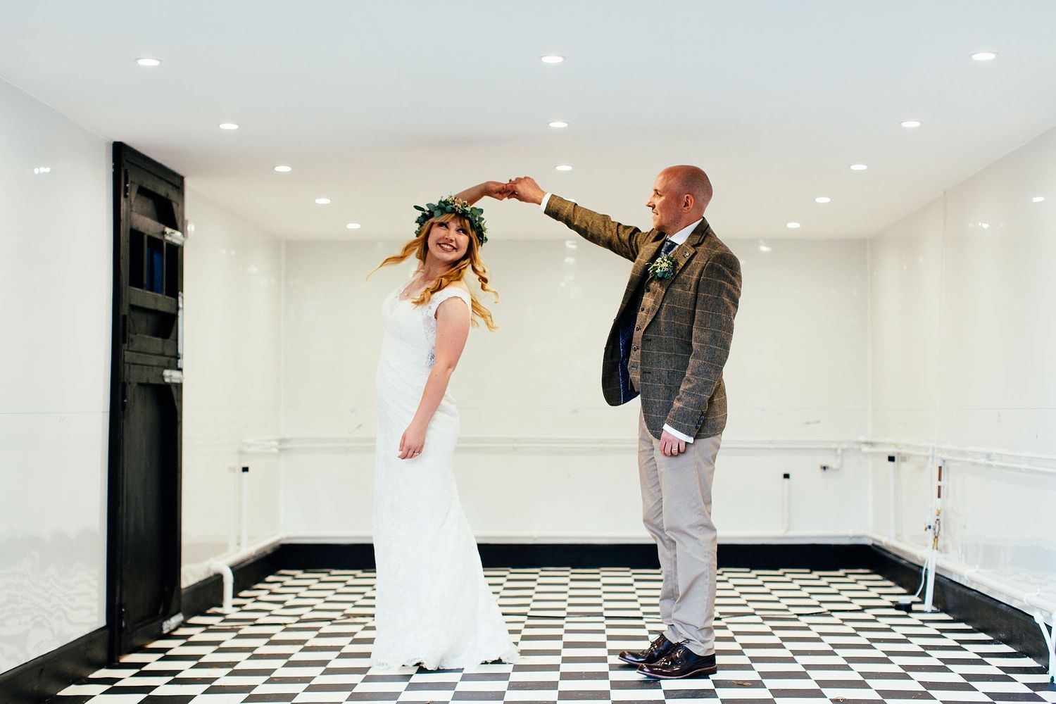 Black and white checkered dance floor in an elegant white reception venue with recessed lighting.