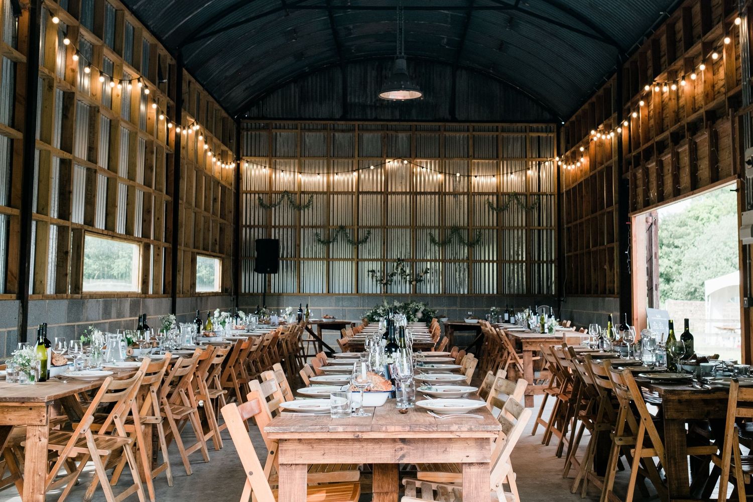 A rustic barn venue set for a wedding reception with string lights and wooden tables.