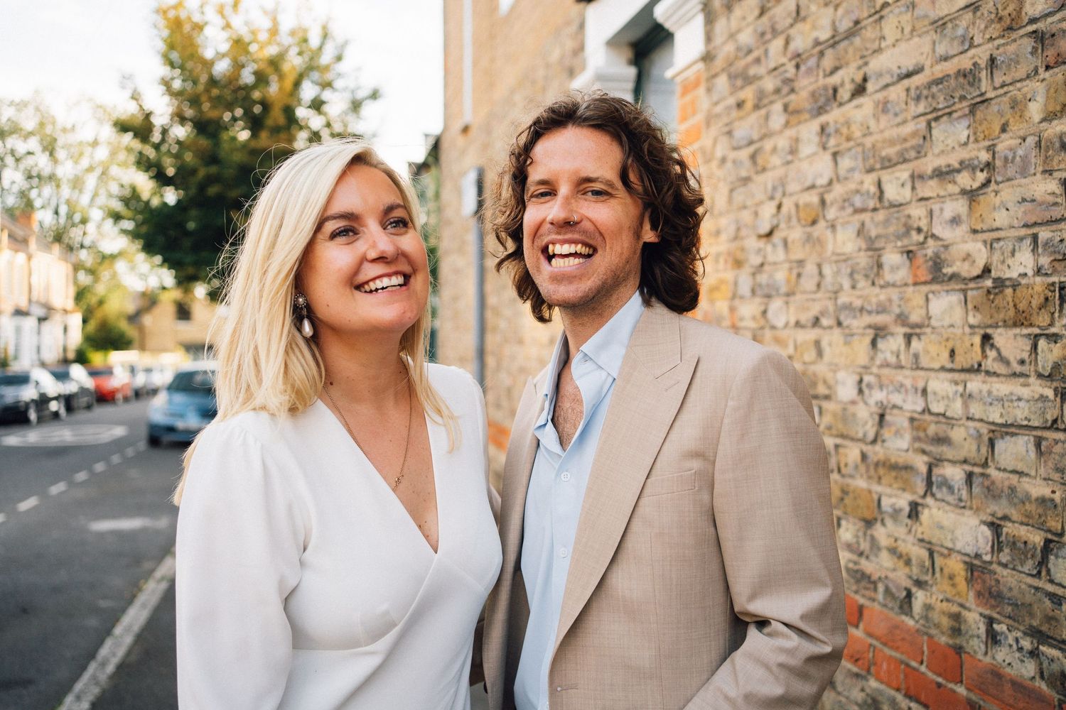 Two people share a joyful moment together while standing against a brick wall on an urban street.