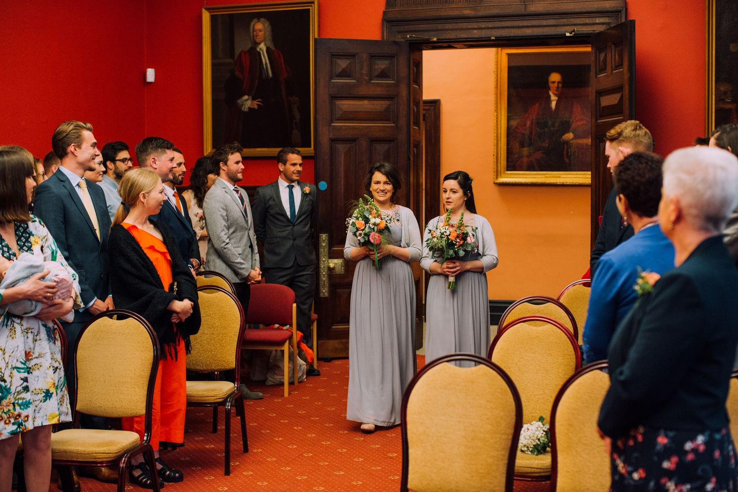 Wedding ceremony in an elegant red-walled room with guests seated in rows.