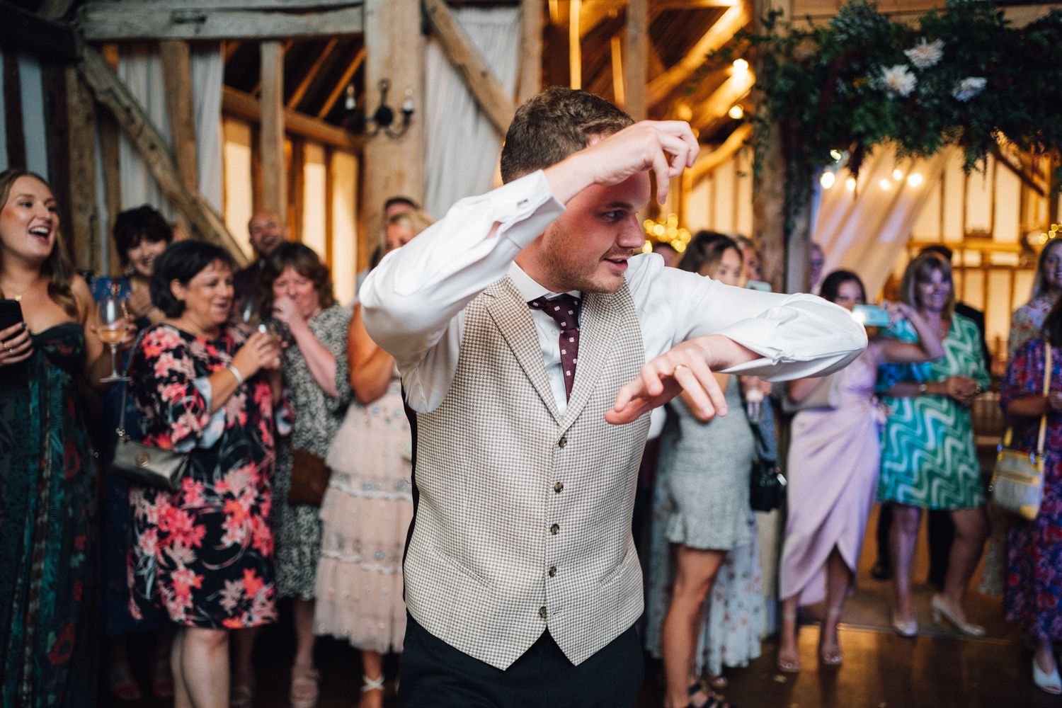 Evening wedding celebration with guests dancing under string lights at a barn venue.