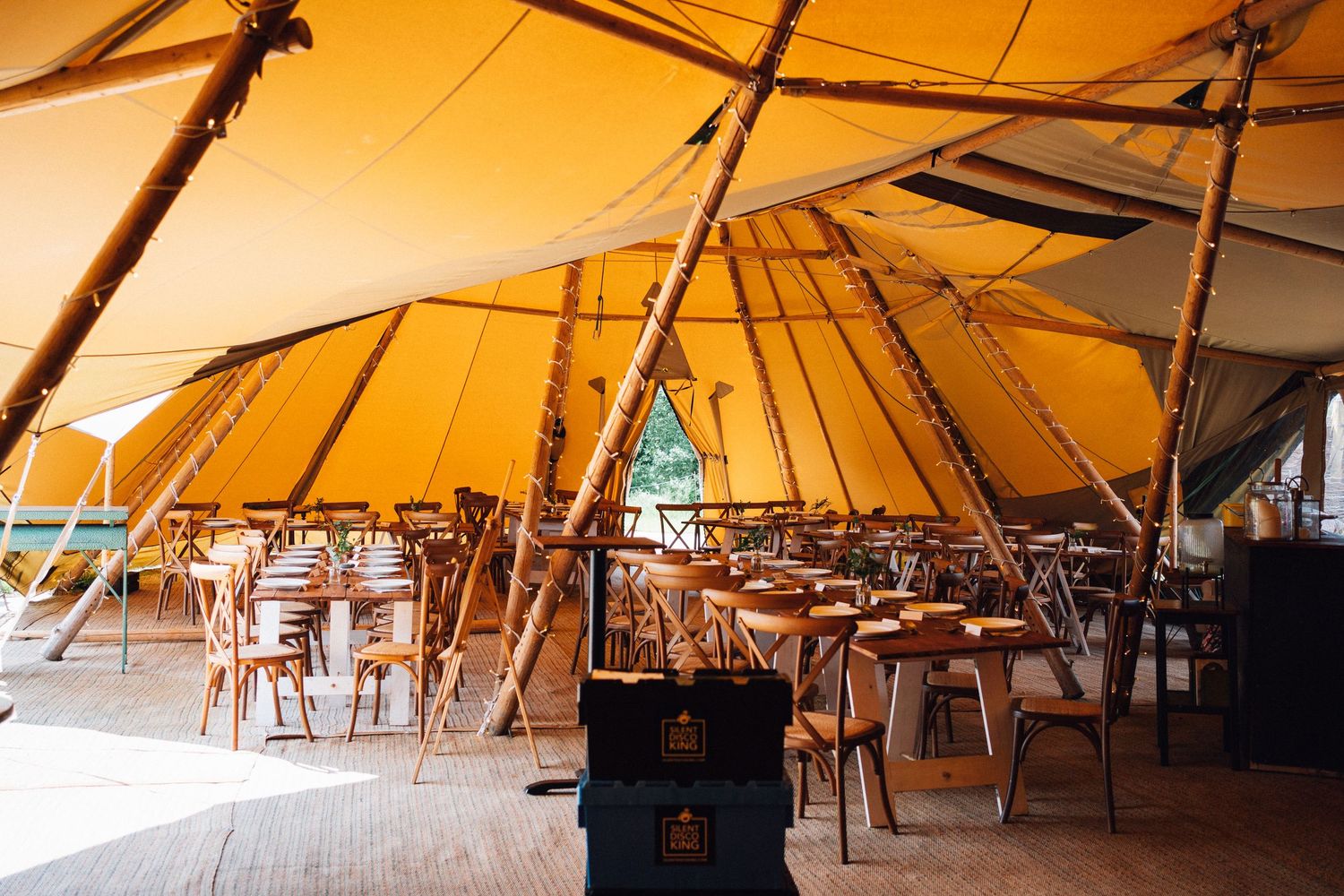 A row of open-air tents with wooden tables and chairs set up for outdoor dining under warm lighting at sunset.