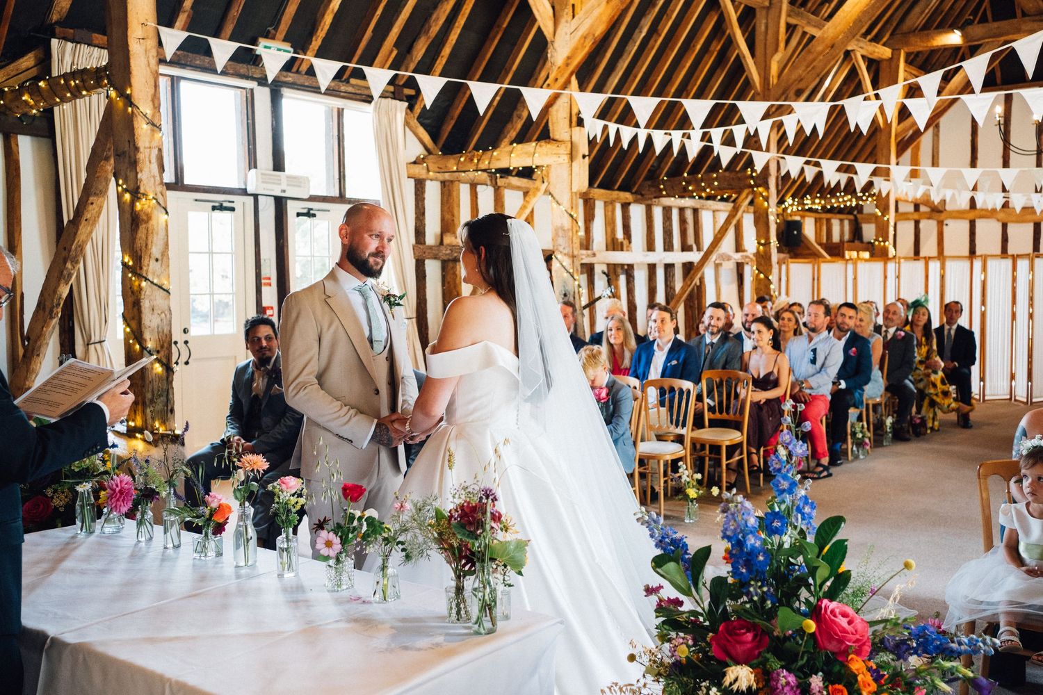 A rustic barn wedding reception venue decorated with white bunting and floral centerpieces on long wooden tables.