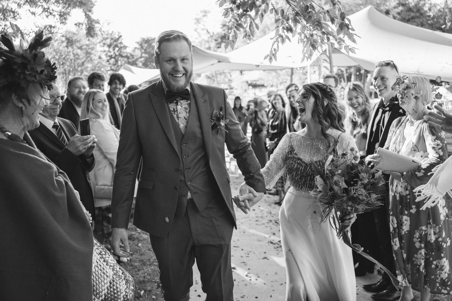 Wedding celebration outdoors with guests gathered under a tent canopy during a sunny afternoon.